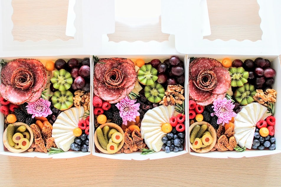Charcuterie boxes featuring cheese, meats, fruits, and vegetables